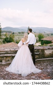 Wedding At An Old Winery Villa In Tuscany, Italy. A Wedding Couple Stands On The Roof Of An Old Winery, Cuddles, Stands With His Back To The Frame.