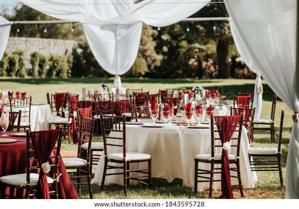Wedding outdoor\
reception - round table with white table cloths, golden plates,\
rustic wooden centerpieces and black candle lanterns, eucalyptus\
leaves and red napkins.