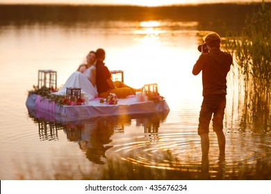 Wedding photographer in action, taking a picture of the bride and groom sitting on the raft. Summer, sunset