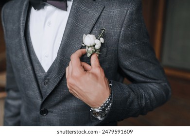 Wedding photography, close-up portrait of the groom in a gray suit, holding a boutonniere with a flower with his hand. - Powered by Shutterstock