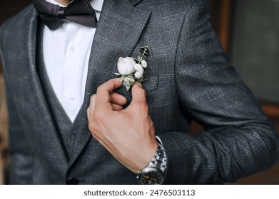 Wedding photography, close-up portrait of a stylish groom in a gray suit, holding a boutonniere with a flower with his hand. - Powered by Shutterstock