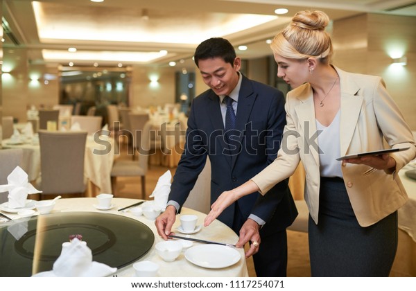 Wedding planner and banquet manager discussing\
table setting