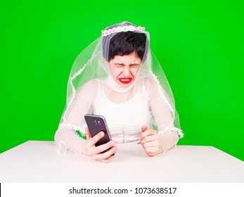 Wedding relationship difficulties. Sad woman with a phone in her hand is crying. Unhappy bride crying sitting at a table on a green background - Powered by Shutterstock