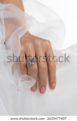 Wedding ring close up with a huge round cut diamond on woman's hand in white tulle.