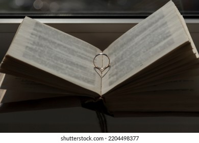 Wedding ring with a falling shadow in the form of a heart standing on an open book... - Powered by Shutterstock