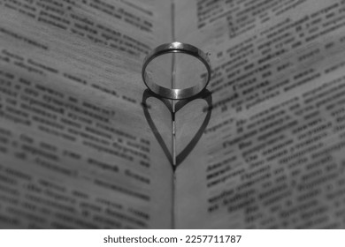 Wedding ring with a falling shadow in the form of a heart standing on an open book... - Powered by Shutterstock