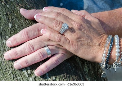 Wedding Ring Hands
An Older Couple Who Just Got Married Shows Off Their Wedding Rings On Their Left Hands. Their Hands Are Placed On A Limb Of A Live Oak Tree. 