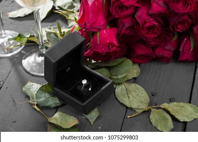 Wedding ring in velvet box with red rose bouquet, champagne and green roses leaves on rustic black wooden background. Engagement conceptual and copy space for text area.  - Powered by Shutterstock