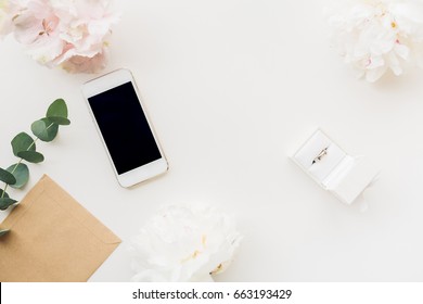 Wedding Ring In A White Gift Box On The Background Of Flowers And Phone. Top View