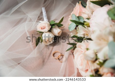 wedding rings and boutonniere lie on the veil next to the bride's bouquet
