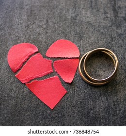 Wedding rings and broken red  heart. Black background. The concept of divorce, parting, infidelity .