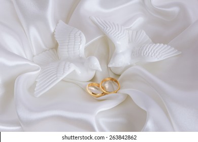 Wedding rings and figurines of doves on white silk