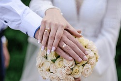 Wedding Rings On The Hands Of The Newlyweds, A Bouquet Of Flowers In The Background. Gold Rings On The Hand Of A Man And A Woman