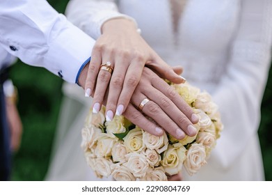 Wedding rings on the hands of the newlyweds, a bouquet of flowers in the background. Gold rings on the hand of a man and a woman