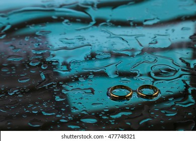 Wedding rings with water drops on a dark green background.