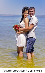 Wedding. Sexy Bride And Casual Groom  Standing In Water. Shore. Love Story Of Happy Couple. Wedding Dress And Umbrella. Bridal Wedding Bouquet Of Flowers.