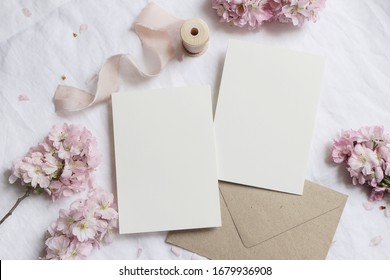 Wedding stationery mock-up scene. Blank greeting cards, envelope on linen tablecloth background with pink blossoming cherry tree branches and ribbon. Feminine still life composition. Flat lay,top view - Shutterstock ID 1679936908