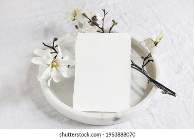 Wedding Stationery Mock-up Scene. Blank Vertical Greeting Card On Marble Tray. White Linen Tablecloth Background With Blooming Magnolia Stellata Tree Branches. Feminine Still Life. Flat Lay, Top View.