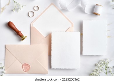 Wedding stationery set. Flat lay wedding invitations, pastel pink envelopes, wax seal stamp, golden rings, flowers on marble desk.  - Shutterstock ID 2125200362