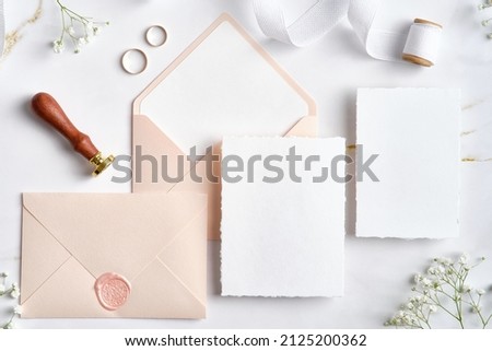 Wedding stationery set. Flat lay wedding invitations, pastel pink envelopes, wax seal stamp, golden rings, flowers on marble desk. 