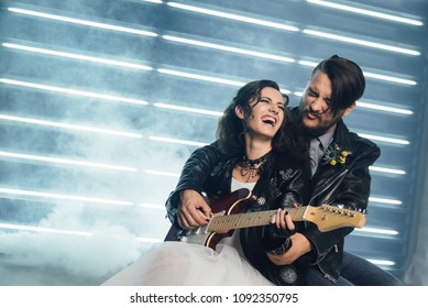 Wedding In The Style Of Rock. Rocker Or Biker Wedding. Guys With Stylish Leather Jackets. It's A Rock'n'roll Baby! Sweet Couple In A Photo Studio. Steep Shooting With Electric Guitar And Smoke.