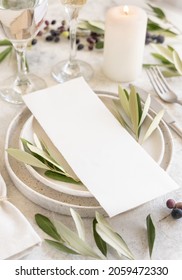 Wedding Table Place With A Menu Card And Porcelain Plates Decorated With Olive Branches Close Up. Elegant Modern Template With Vertical Blank Paper Card. Mediterranean Flat Lay Mockup, Copy Space