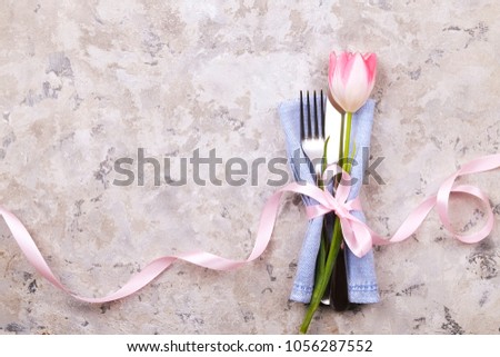 Wedding table setting composition with fork & knife silverware, pink tulip tied w/ pink ribbon, grey stucco plaster background. Easter celebration. Greeting, Close up, template, top view, copy space.