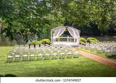 Wedding Venue Next To A Pond And Forest With White Chairs And A White Gazebo And A Brick Isle. 