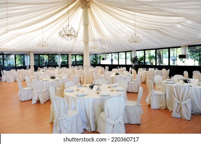 Wedding Venue Under A Marquee With Decorated Tables And Chairs Draped In White Linen Around A Central Pole Supporting The Canvas