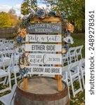 A wedding welcome sign on a barrel with floral decorations and white chairs in an outdoor setting in Elkhart County, Indiana