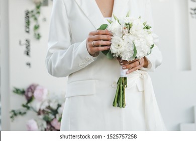 Wedding White Bouquet In The Hands Of The Bride. The Bride In A Pantsuit.