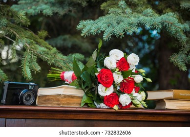 a wedding white and red roses bouquet laying on the piano near the old books and old camera.  pine-tree on the background.  wooden rustic style.  olf fashion.  - Powered by Shutterstock