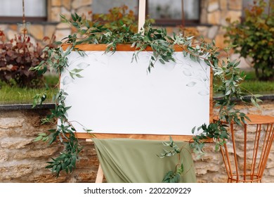 Wedding Wooden Board, Mockup, Invitation Easel, With White Space For An Inscription, Decorated With Fresh Greenery And Green Cloth. Wedding Frame Outdoors. Festive Decor, Copy Space