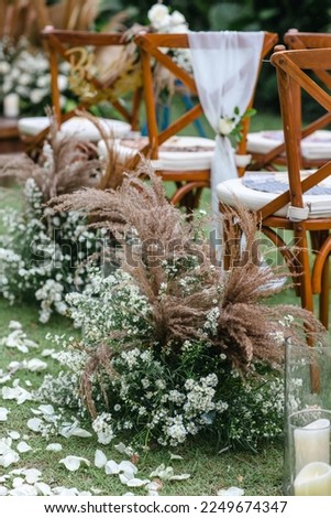 Wedding wooden chairs decorated with dry flowers. Rustic aisle chairs standing on lawn for ceremony in garden. Natural, shabby, boho wedding decor concept