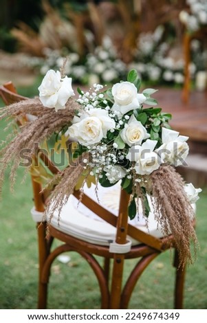 Wedding wooden chairs decorated with flowers. Rustic aisle chairs standing on lawn for ceremony in garden. Natural, shabby, boho wedding decor concept