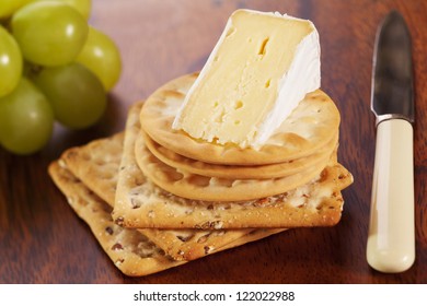 A Wedge Of Brie Cheese With Crackers And Grapes.