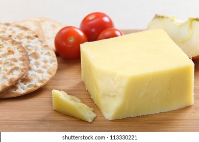 A Wedge Of English Cheddar Cheese With Crackers And Cherry Tomatoes On A Cheeseboard