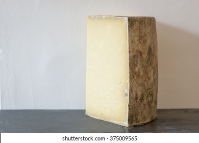 A Wedge Of Montgomery's Cheddar On Slate And White Wall Behind