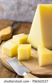 Wedge Of Spanish Cured Hard Goat Cow And Ewe Cheese Cut In Cubes On Wood Platter. Knife And Fork On Table. Traditional Appetizer, Tapas, Mediterranean Cuisine.