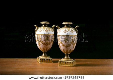 A Wedgwood lilac Jasper two-handled, Campagna urn and cover with a pair of early 20th century Wedgwood Etruria, two-handled classical, porcelain urns. Photographed on wood with a black background.