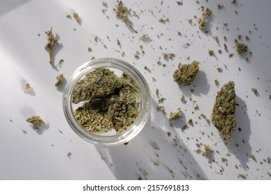 Weed Store. Glass Jar With Dried Cannabis Buds On White Background With Crushed Marijuana.