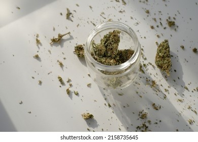 Weed Store. Glass Jar With Dried Cannabis Buds On White Background With Crushed Marijuana.