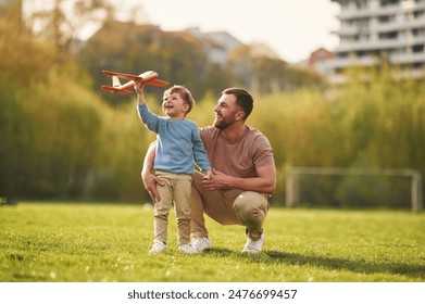 Weekend activities. Playing with toy plane. Happy father with son are having fun on the field at summertime.