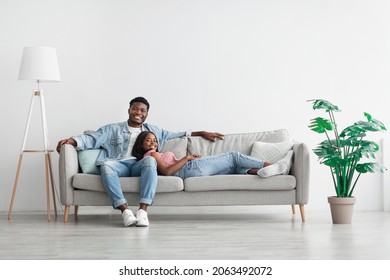 Weekend. Beautiful African American woman and handsome man relaxing on couch at home in living room, smiling couple looking at camera, posing, spending leisure time together, lady lying on guy's lap