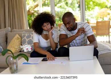 Weekend Fun At Home Together. Front View Of A Mixed Race Couple Sitting In The Living Room On The Couch, Using A Laptop Computer Together And Looking At Paperwork