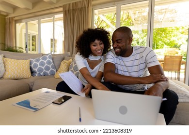 Weekend Fun At Home Together. Front View Of A Mixed Race Couple Sitting In Their Living Room, Using A Laptop Computer Together And Smiling 