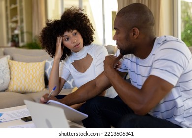 Weekend Fun At Home Together. Side View Of A Mixed Race Couple Sitting In The Living Room Using A Tablet And A Laptop Computer And Talking, With Serious Expressions