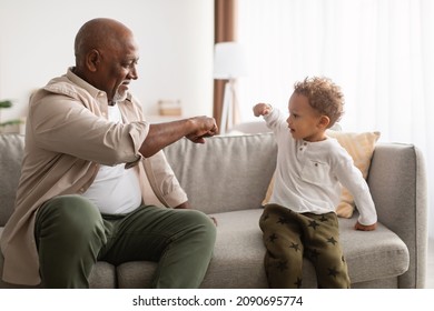 Weekend With Grandfather. Happy Black Grandpa And Little Grandson Bumping Fists Sitting On Sofa At Home. Senior Man And His Grandchild Doing Fist Bump Greeting Gesture.