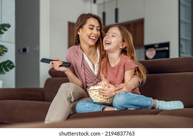 Weekend at home. Cute little girl watching TV with her mom, eating popcorn-copy space. - Powered by Shutterstock