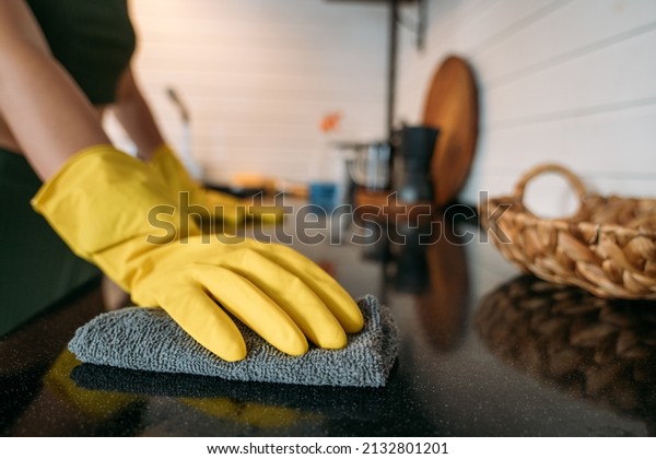 Weekend homework. A woman is cleaning the kitchen
at home. Close-up of hands in yellow gloves cleaning the
countertop, working kitchen
surface